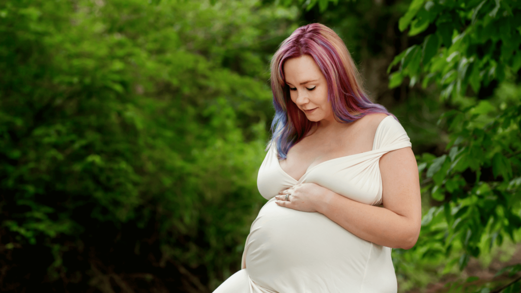 Pregnant mom sitting outside looking down at her bump.